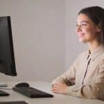 Personne assise à un bureau face à un ordinateur, souriante.